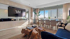 Een moderne woonkamer met een flatscreen televisie, een houten salontafel en een eethoek met stoelen en een tafel.