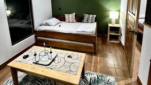 Un dormitorio con cama, mesita de noche, lámpara y ventana.