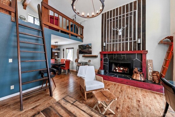 Un salón tipo loft con chimenea, suelo de madera y cama en un altillo.
