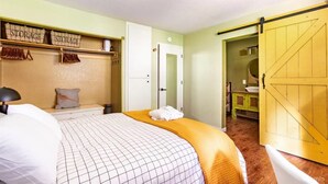 Une chambre à coucher comprenant un lit, un meuble de rangement, une armoire et une salle de bain visible à travers une porte ouverte.