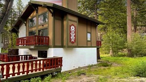Une cabane à deux étages avec un balcon, entourée d’arbres.