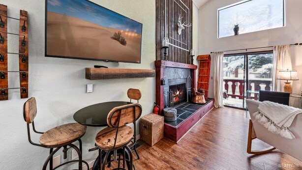 Un salon chaleureux avec une cheminée, un grand téléviseur et un coin repas avec des chaises en bois.