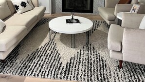 Een moderne woonkamer met een open haard, twee banken, een salontafel en decoratieve items op planken.