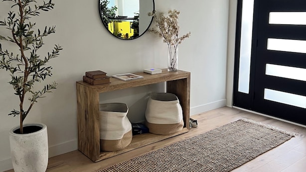 Een kamer met een houten console tafel, een grote spiegel, een potplant en een geweven vloerkleed.