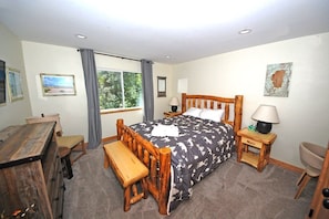 Une chambre à coucher avec un lit en bois, un bureau, une chaise, un banc et une fenêtre avec des rideaux.
