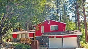 Una casa roja de dos pisos con un garaje, rodeada de árboles.