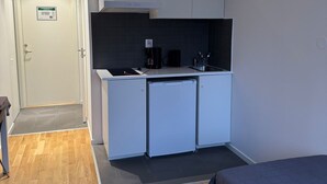 Pieni huone, jossa on pieni keittiönurkkaus, sänky ja pieni työpöytä.