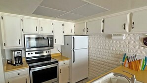 A compact kitchen with white cabinets, a microwave, a refrigerator, an oven, a sink, and a coffee maker.