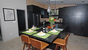 A modern kitchen with a central island, black cabinets, and a dining area with four chairs and a table set for four. - Penthouse Retreat with Mountain Views & Designer Touches (South Lake Tahoe)