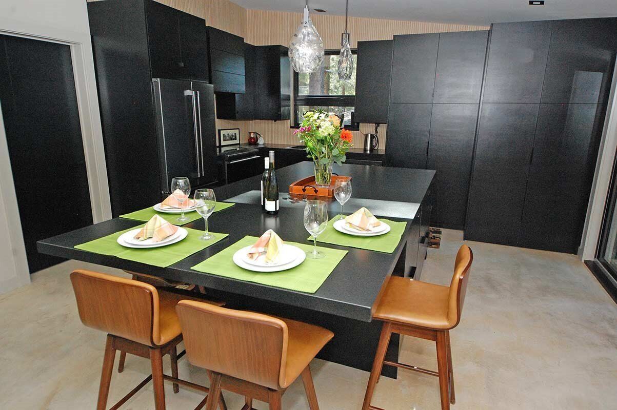 Une cuisine moderne avec des meubles de couleur noire, un îlot central et un coin repas comprenant quatre chaises et une table dressée pour quatre personnes.