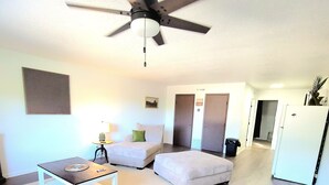 Una sala de estar moderna con ventilador de techo, un sofá blanco, una mesita y un refrigerador blanco.