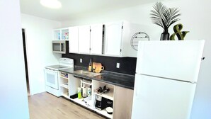 Una cocina compacta con armarios blancos, microondas, estufa y refrigerador.