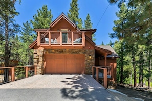 A two-story log cabin with a stone foundation, a large garage, and a balcony.