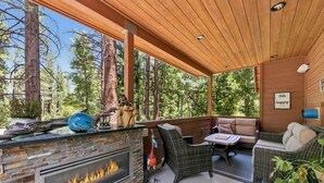 Un espace extérieur abrité, doté d’une cheminée en pierre, de meubles en osier et offrant une vue sur la forêt.