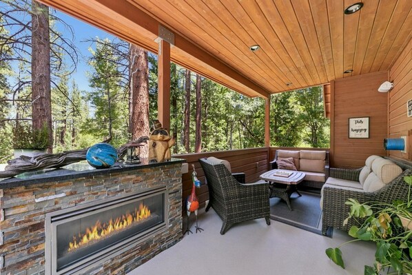 Un espacio al aire libre cubierto con una chimenea de piedra, mobiliario de mimbre y vistas al bosque.