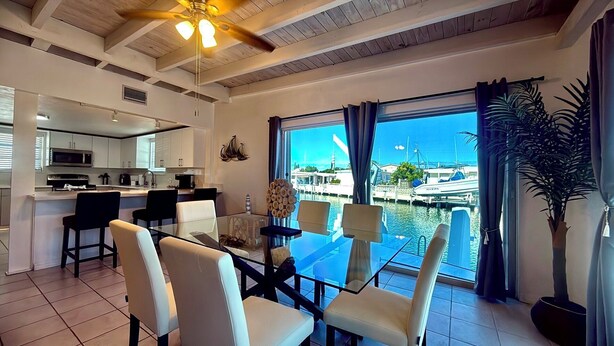 A modern kitchen with white cabinets and stainless steel appliances, a dining area with a glass table and chairs, and a view of a marina with boats. - Paradise House a Waterfront Oasis : Your Perfect Getaway on the Atlantic! (Marathon)