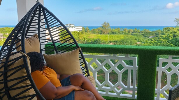 A person relaxing in a hanging chair with a view of a lush green landscape and the ocean. - Nova Stays 1-Bedroom Apartment with Private Pool & Uninterrupted Seaview (Mombasa)