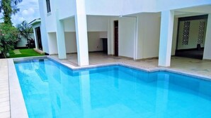 A swimming pool with a tiled deck, a covered patio area, and a view of a white building. - Nova Stays 1-Bedroom Apartment with Private Pool & Uninterrupted Seaview (Mombasa)