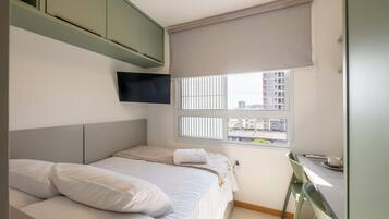 Un dormitorio con cama, una mesita y una ventana con persianas.