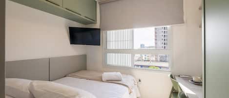 A bedroom with a bed, a small table, and a window with blinds.