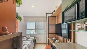 A compact hotel room with a bed, a small kitchenette, a microwave, and a window with blinds. - Your Complete Stay in Salvador, Steps From the sea - Saas (Salvador)