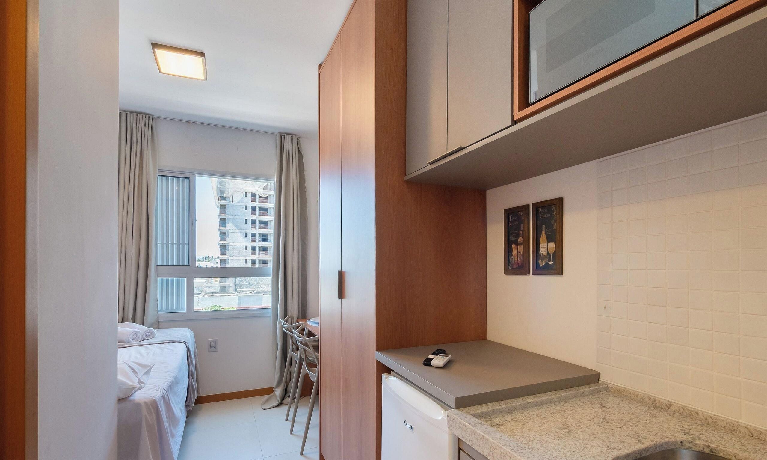 Habitación de hotel compacta con cama, kitchenette pequeña, zona de comedor con mesa y sillas, y ventana con cortinas.