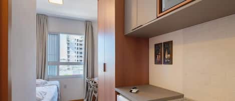 Habitación de hotel compacta con cama, kitchenette pequeña, zona de comedor con mesa y sillas, y ventana con cortinas.