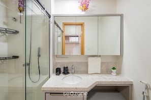 A modern bathroom with a glass shower enclosure, a white sink, and a large mirror above the vanity. - Your Complete Stay in Salvador, Steps From the sea - Saas (Salvador)