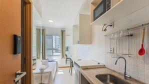A compact hotel room with a kitchenette, a bed, and a view of the cityscape. - Your Complete Stay in Salvador, Steps From the sea - Saas (Salvador)