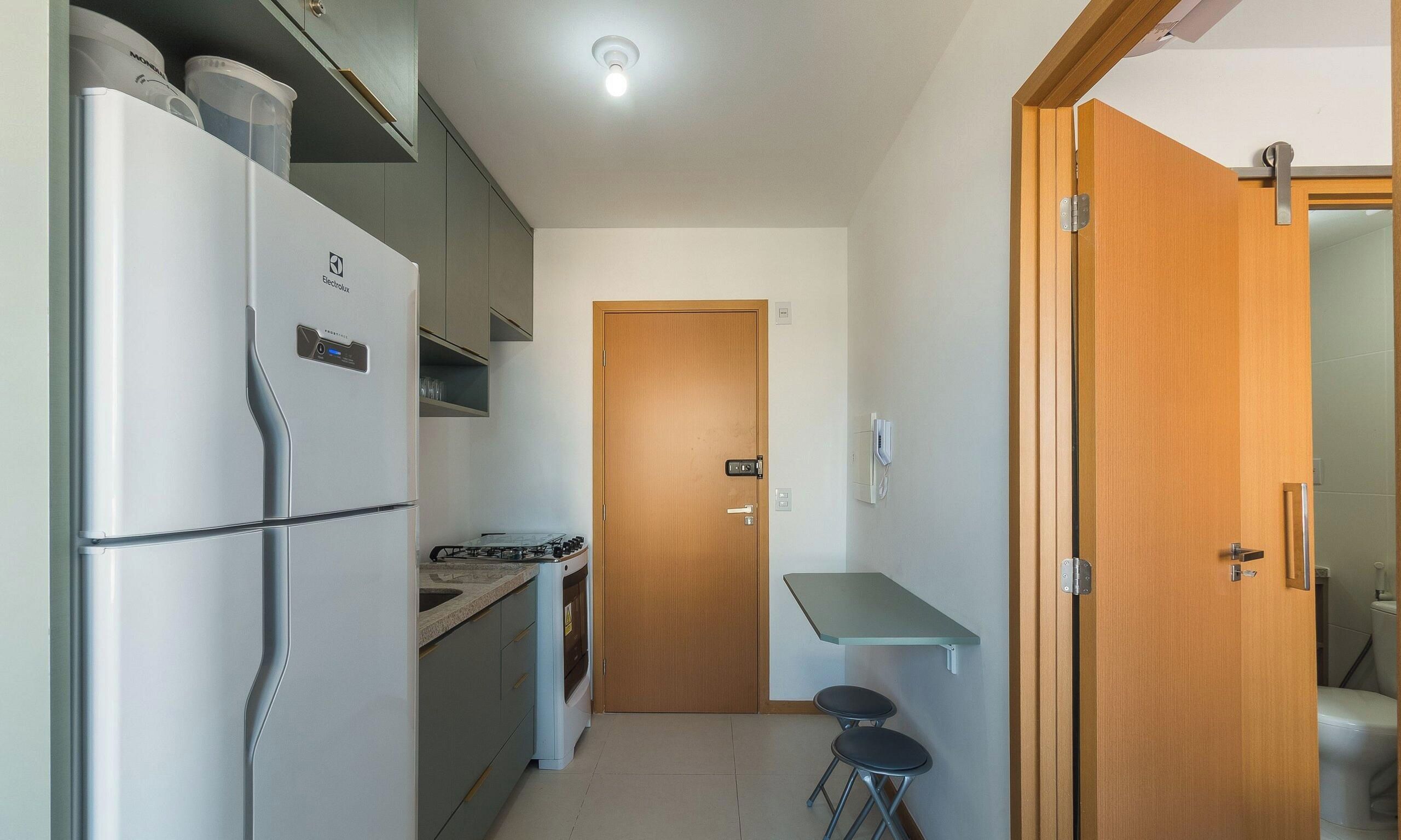 A compact kitchen with a refrigerator, stove, and a wooden door leading to a bathroom.