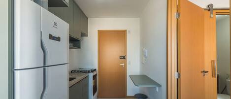 A compact kitchen with a refrigerator, stove, and a wooden door leading to a bathroom.