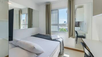 Habitación de hotel con cama, escritorio, silla, espejo y ventana con cortinas.