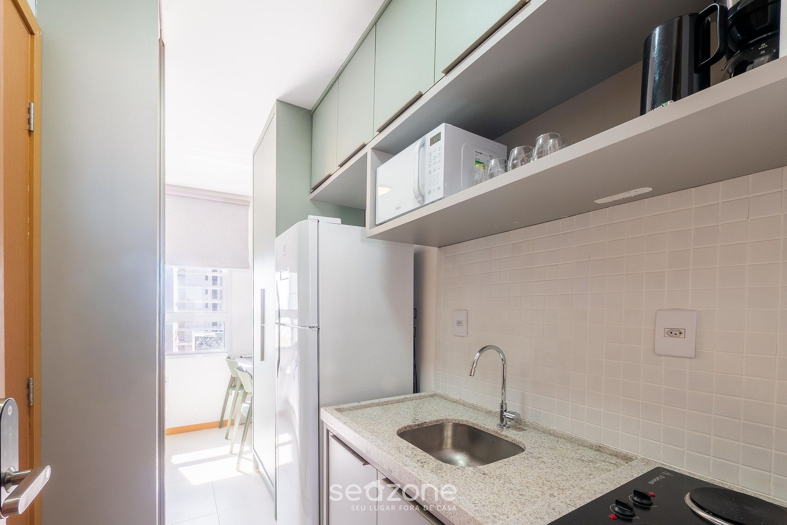 A modern kitchen with white cabinets, a stainless steel sink, and a window overlooking a balcony.