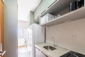 Eine moderne Küche mit weißen Schränken, einer Spüle aus Edelstahl und einem Fenster mit Blick auf einen Balkon.