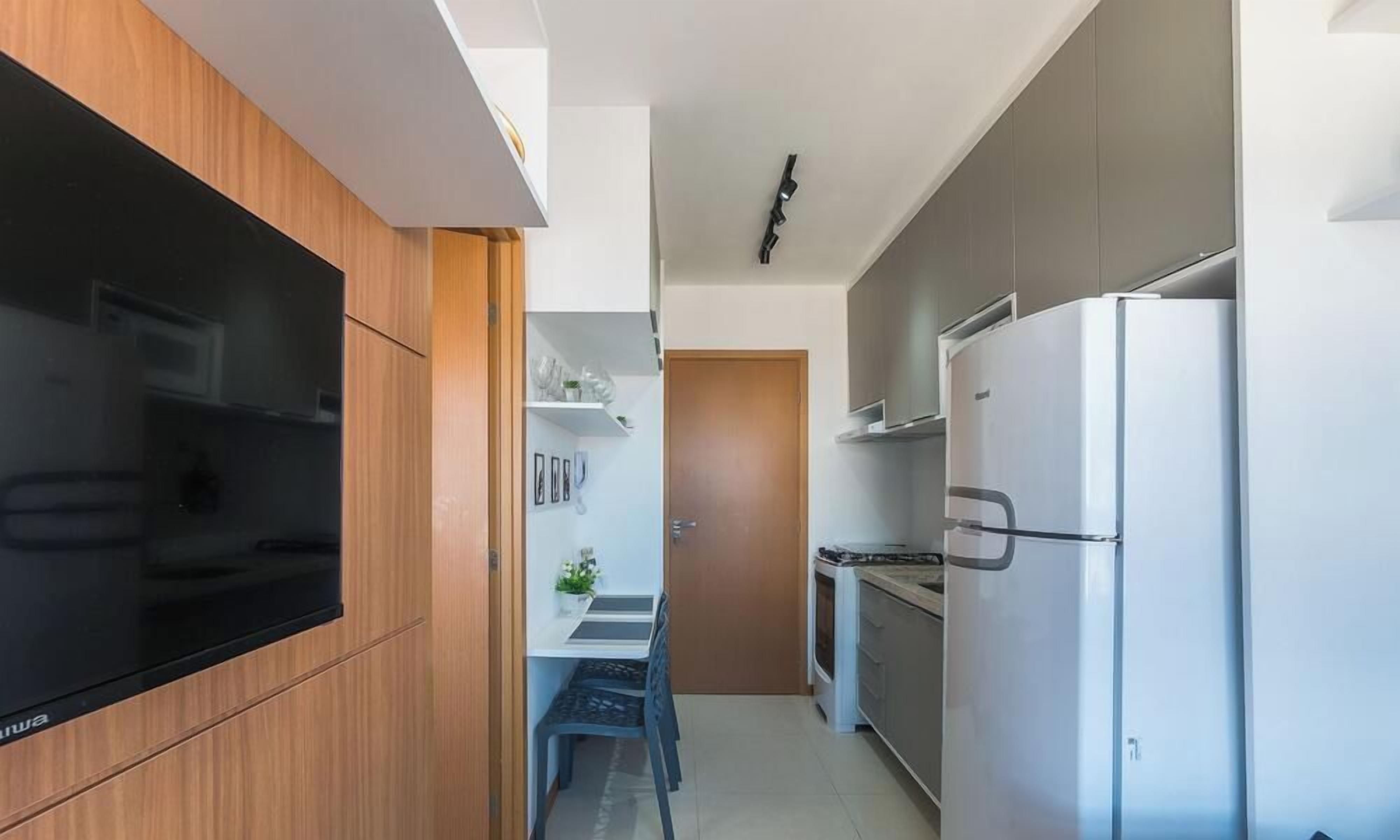 A modern kitchen with a built-in oven, a large refrigerator, and a flat-screen TV mounted on the wall.