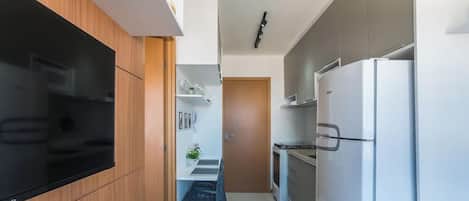 A modern kitchen with a built-in oven, a large refrigerator, and a flat-screen TV mounted on the wall.