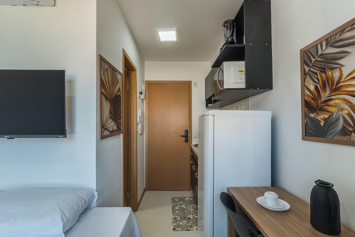 Ein gemütliches Hotelzimmer mit Bett, einem kleinen Tisch mit Tasse und Blumenvase, einem Kühlschrank, einer Mikrowelle und einem an der Wand befestigten Fernseher.