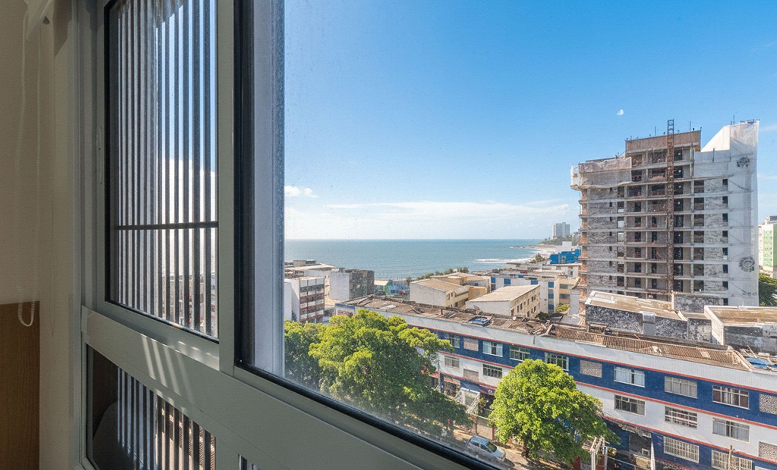 Vista desde una ventana sobre un paisaje urbano costero con edificios y un cielo despejado.