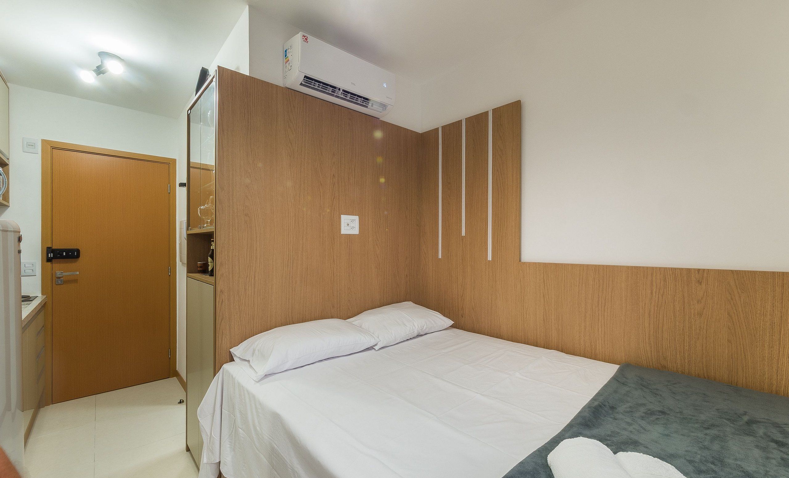 A hotel room with a bed, a wardrobe, a mirror, and an air conditioning unit.
