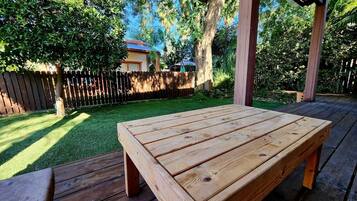 Una terraza de madera con un banco y una mesa, rodeada por una valla de madera y abundante vegetación.