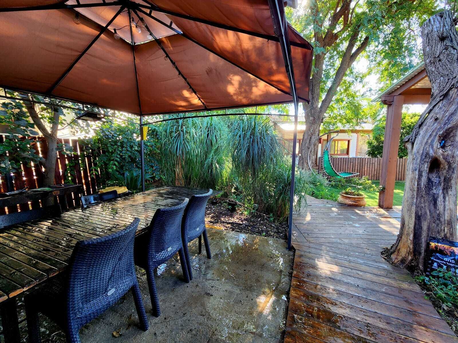 An outdoor patio with a table and chairs, a wooden deck, and a tree.