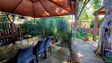 An outdoor patio with a table and chairs, a wooden deck, and a tree.