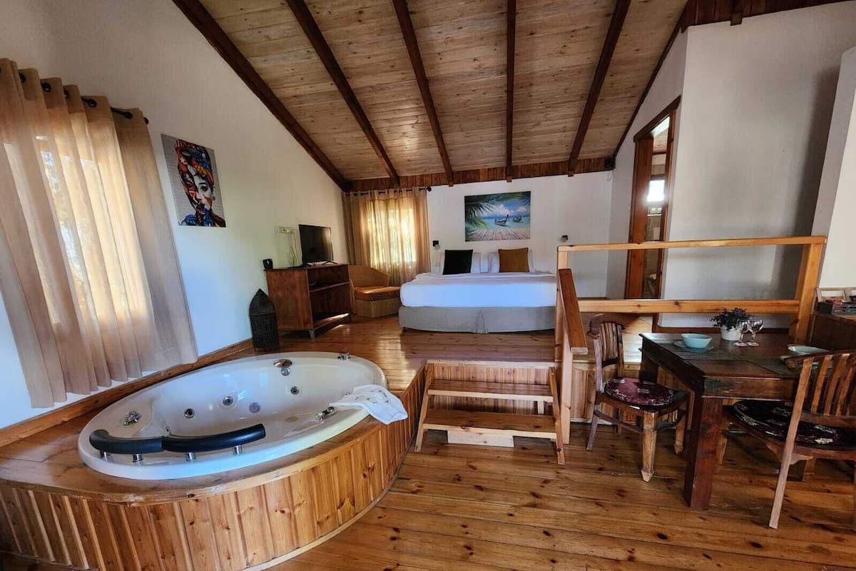 Une pièce au plancher de bois, dotée d’un grand jacuzzi, d’un lit, d’une table à manger avec des chaises et d’un tableau accroché au mur.
