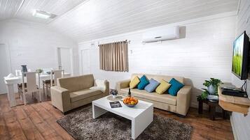 A modern living room with a white sofa, coffee table, and a TV on the wall.