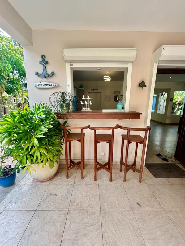 Una zona de recepción con un escritorio y sillas de madera, un cartel que dice 'WELCOME' y plantas en macetas.