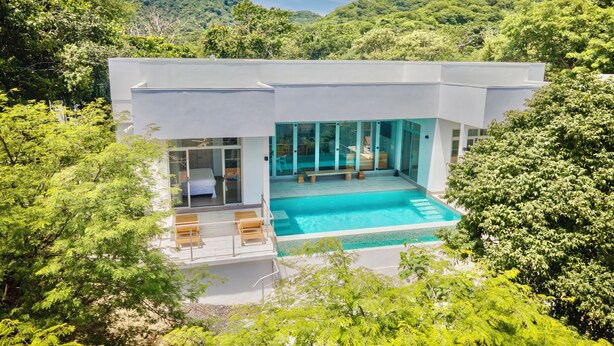 Ein modernes Haus mit Schwimmbad, umgeben von üppiger Vegetation und Hügeln.
