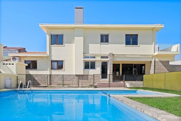 A two-story house with a swimming pool, a covered patio, and a stone wall.