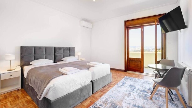A hotel room with a large bed, a desk, a chair, a TV, and a view of the city. - Villa 7BR/7BA with Pool & Backyard Prime Location! (Vila Nova de Gaia)