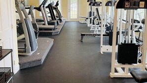 Et fitnessrum med løbebånd, styrkemaskiner og en loftsvifte.