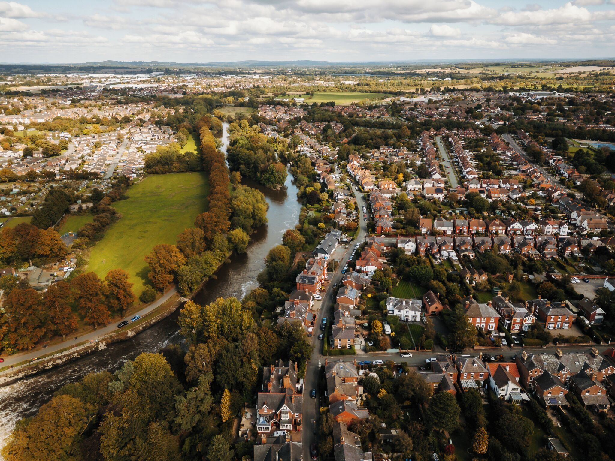 An aerial view of a residential area with houses, a river, and a park.